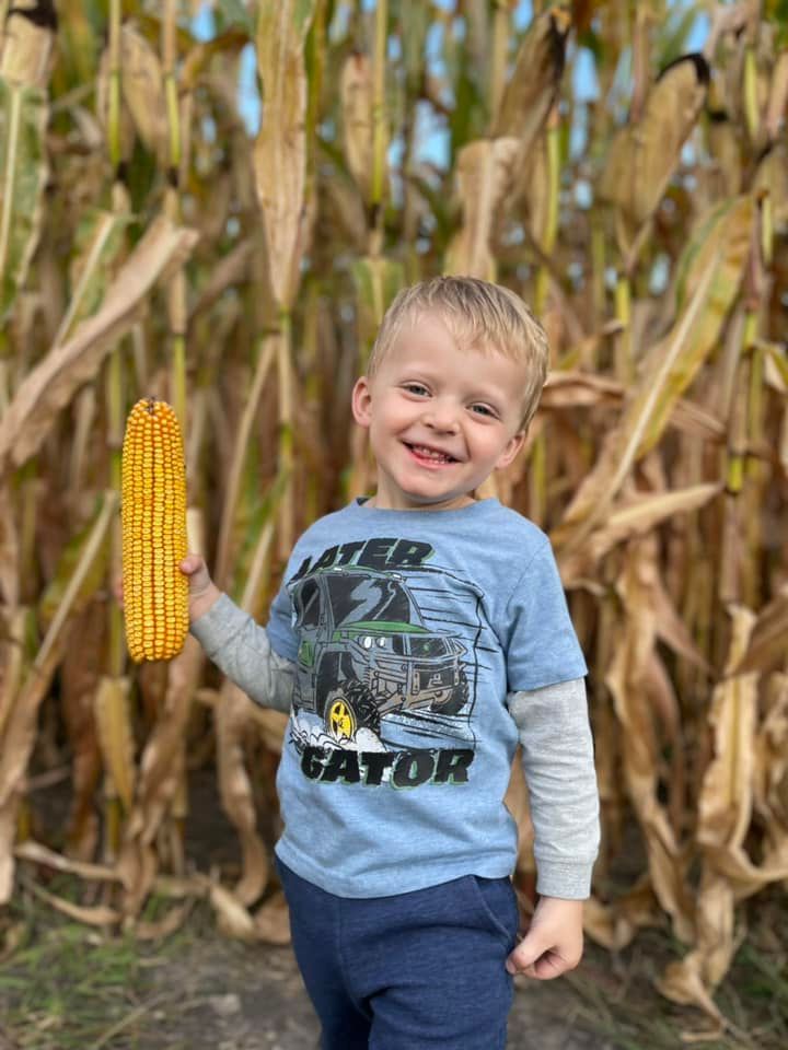 a kid holding an ear of field corn during harvest