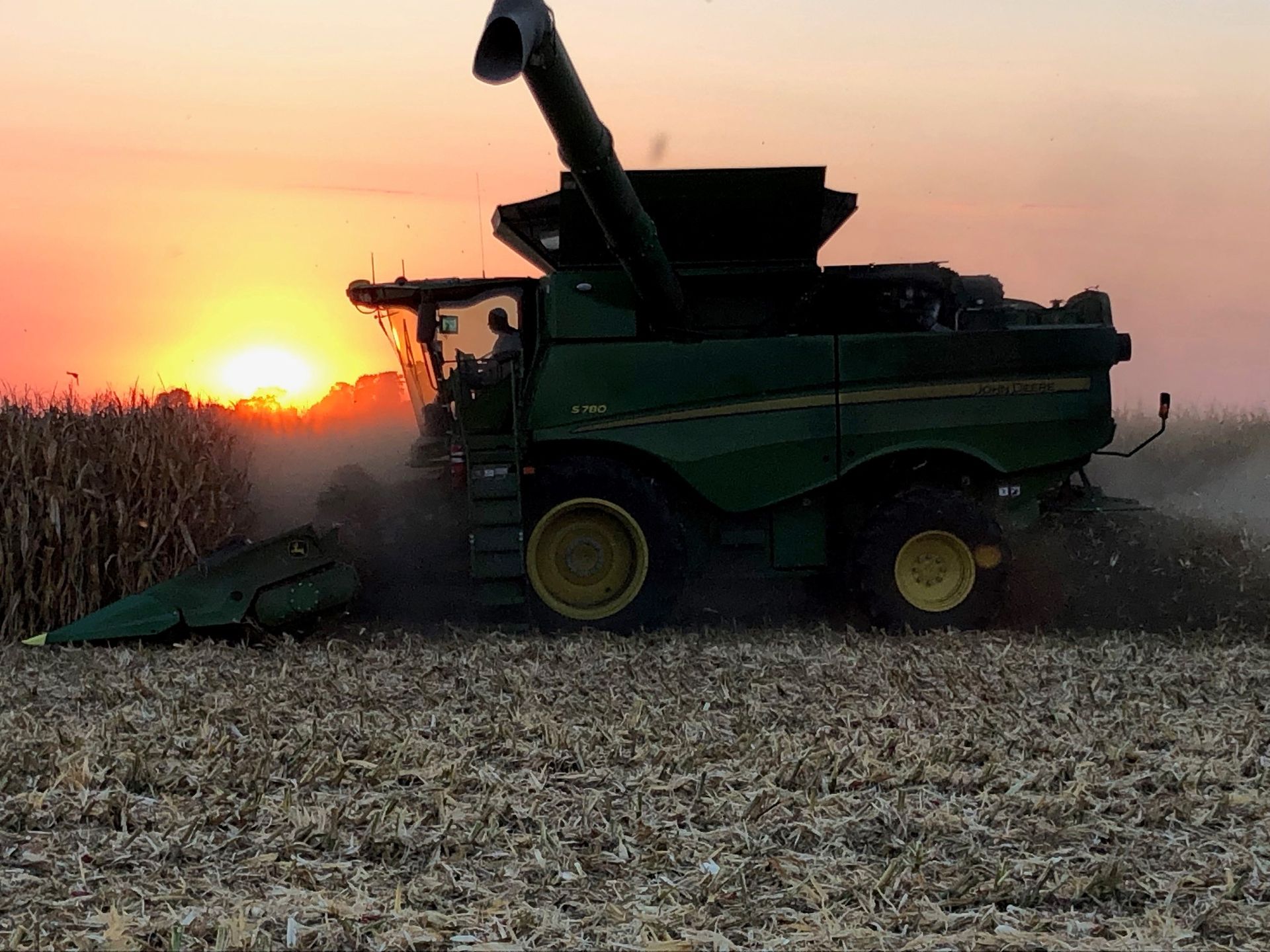 Green combine harvester in a field at sunset, with the sun low on the horizon.