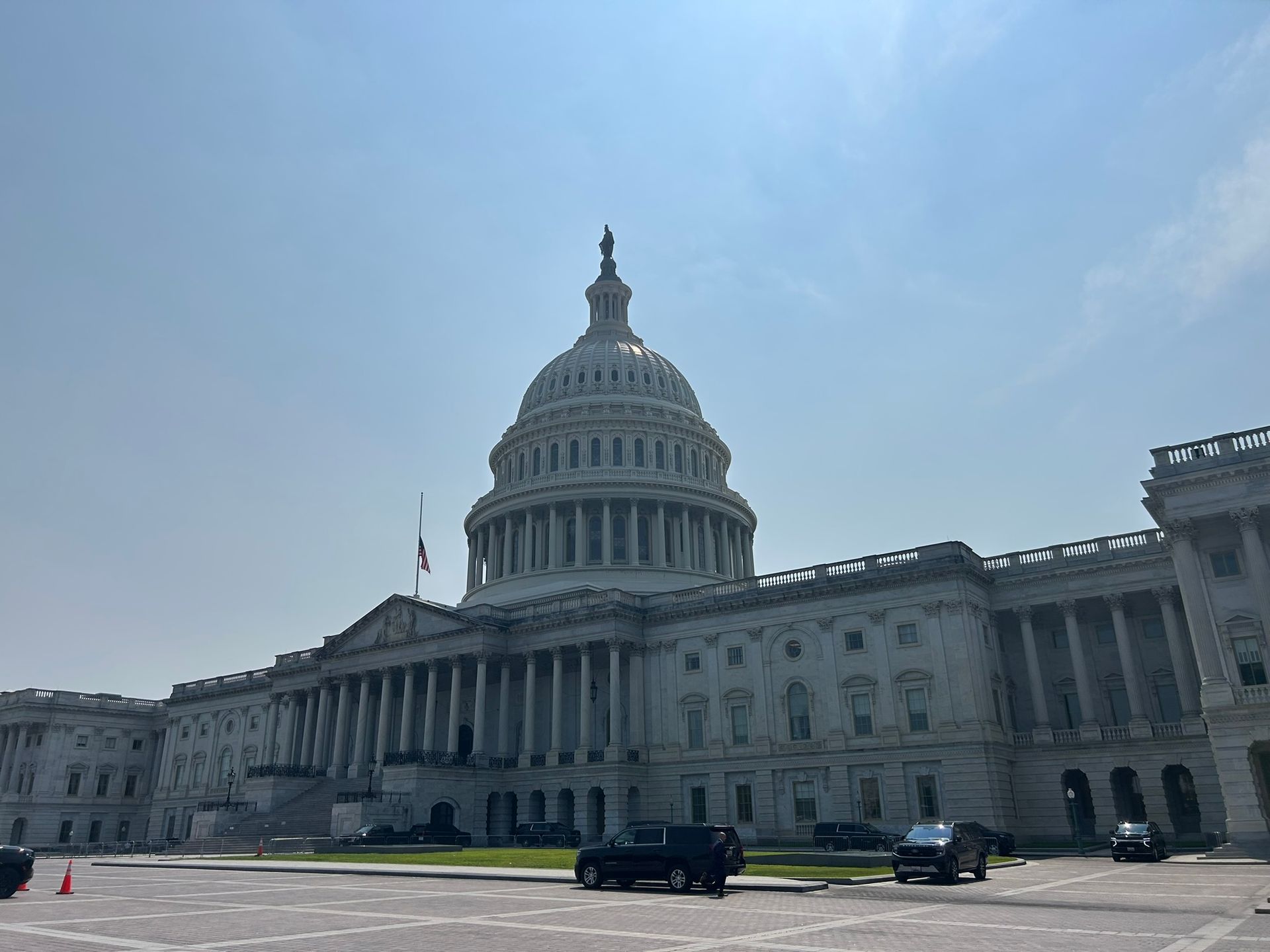 U.S. Capitol building under a bright blue sky, with cars in front on a sunny day
