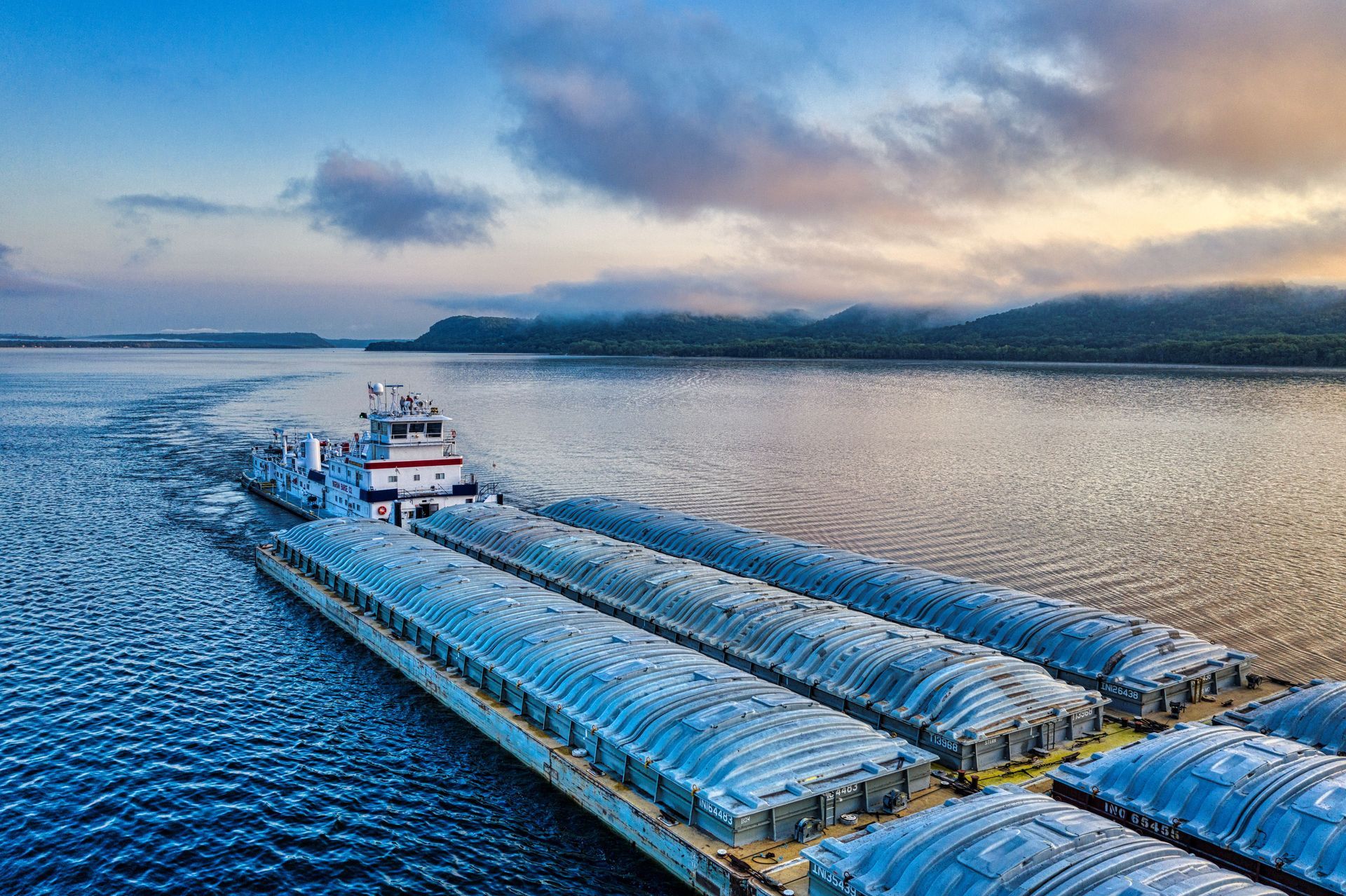 Cargo ship pushing barge convoy across calm blue water at sunset