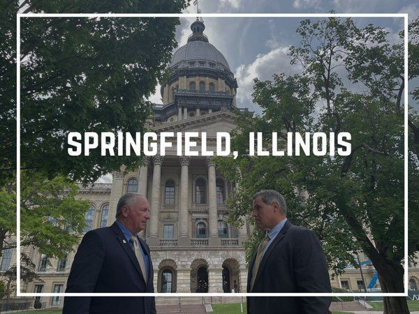 Two men in suits in front of the Illinois State Capitol building in Springfield.