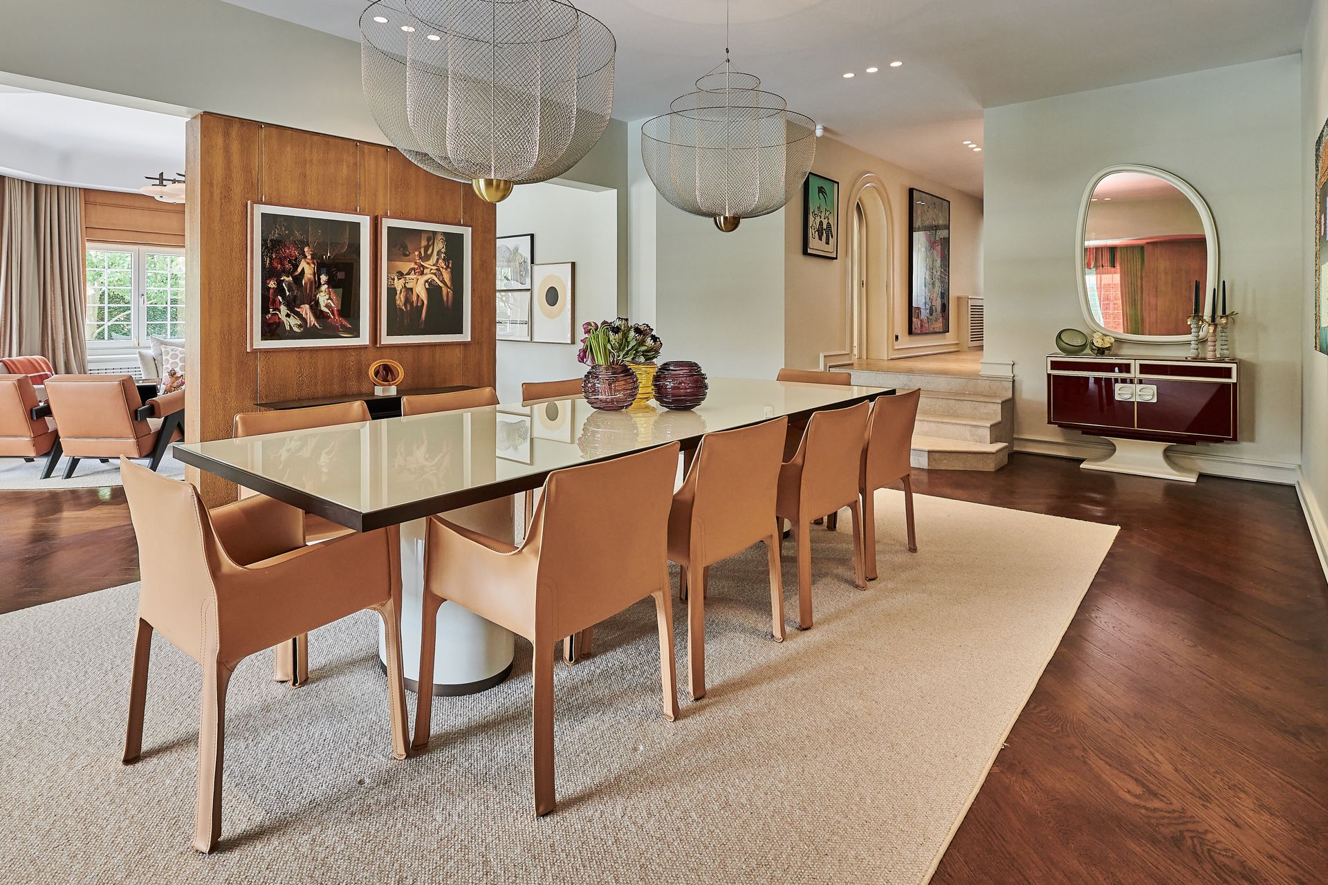 Modern dining room with a glass table, tan chairs, hardwood floors, and decorative wall art.