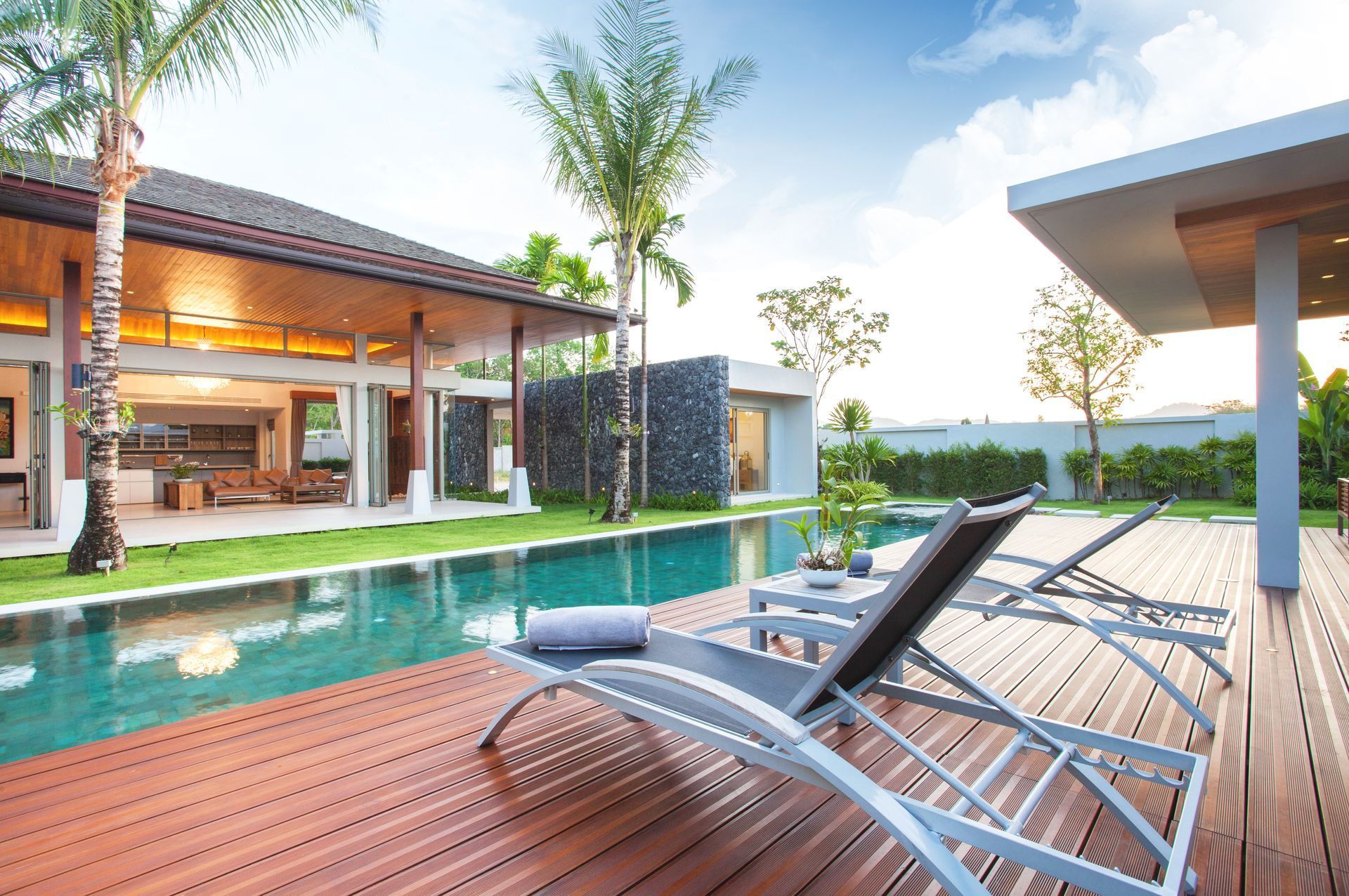 Modern villa with turquoise pool, wooden deck, lounge chairs, and palm trees at sunset