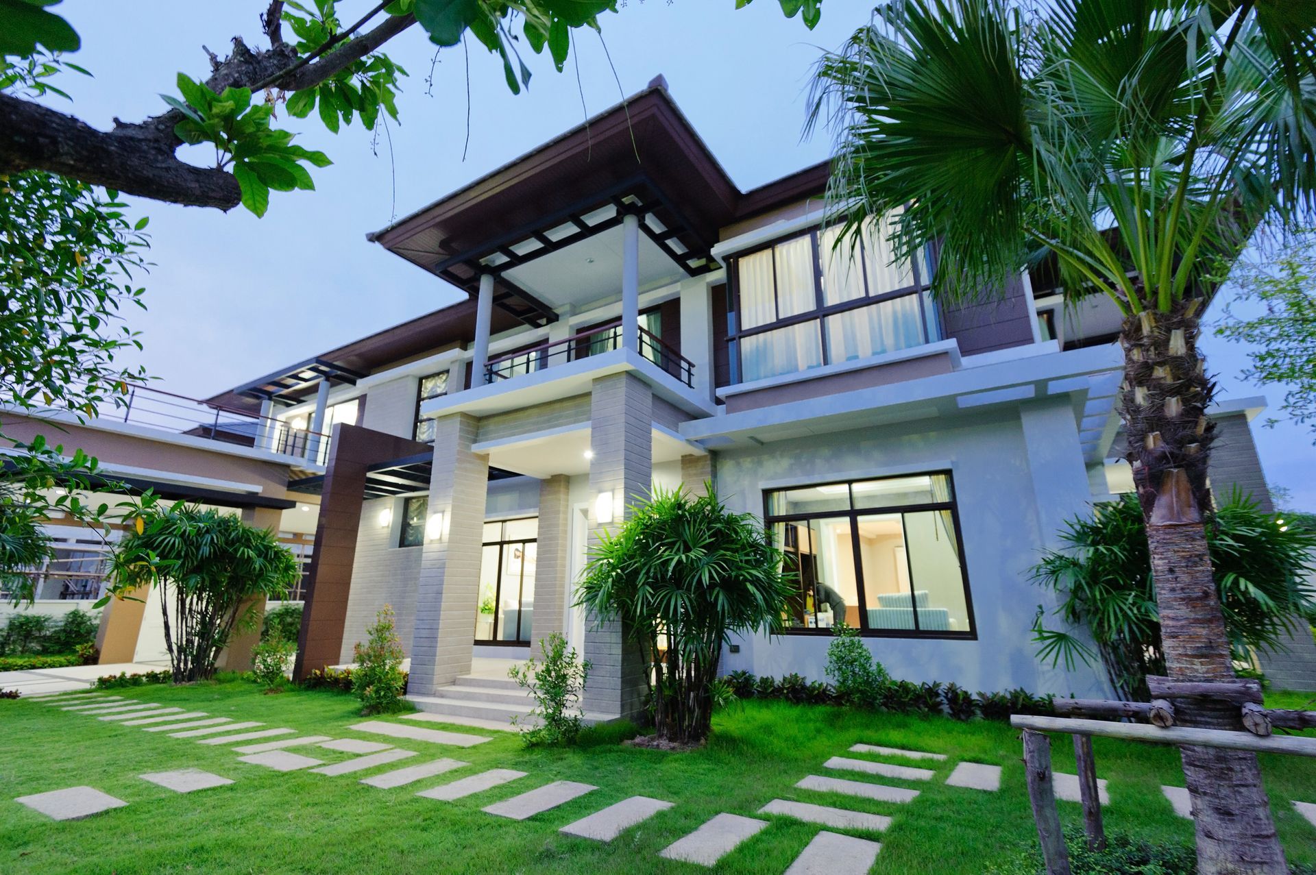 Modern two-story white house with a lush green lawn, palm trees, and a covered porch at dusk