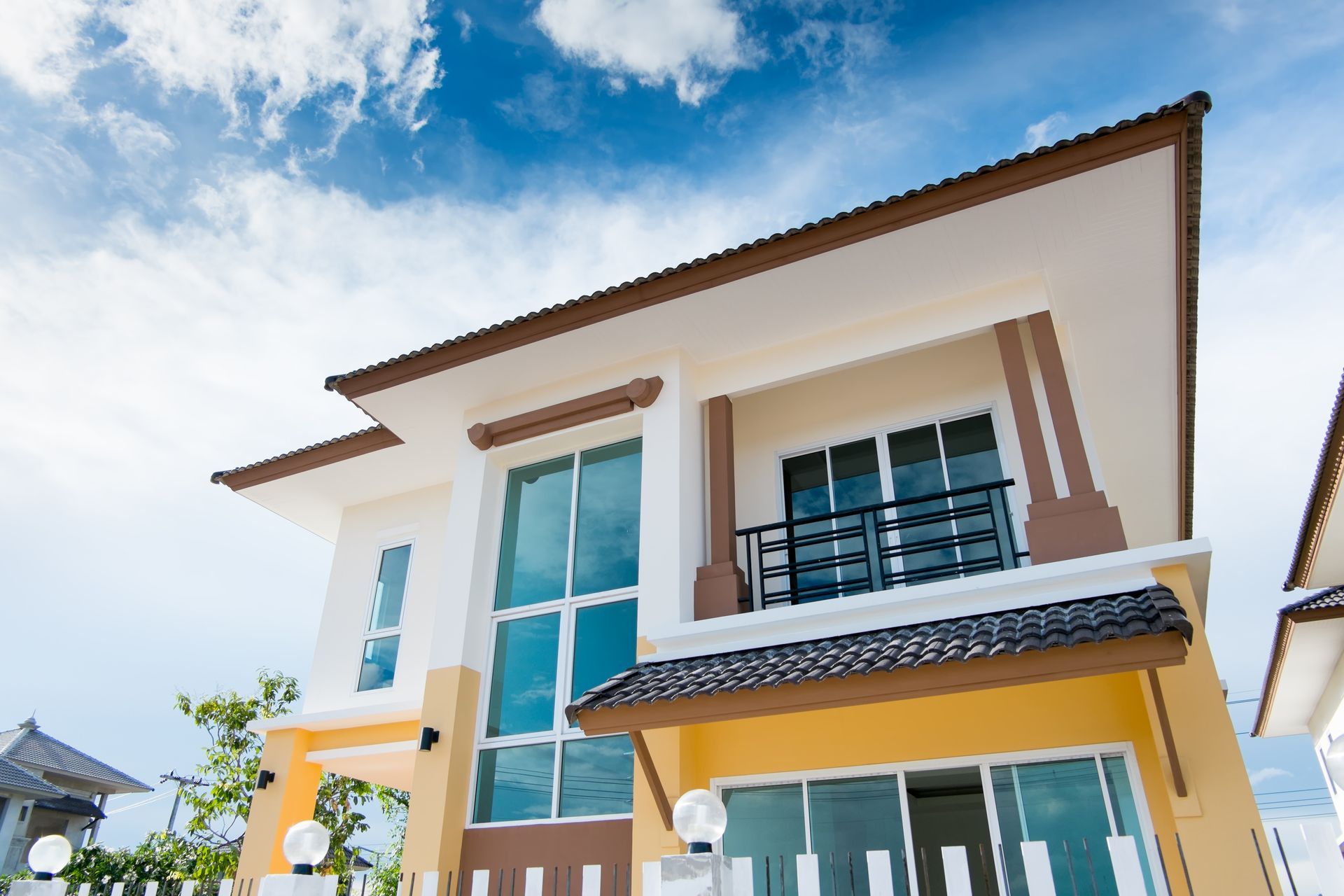 Modern two-story house with white walls, brown trim, blue windows, and a bright blue sky