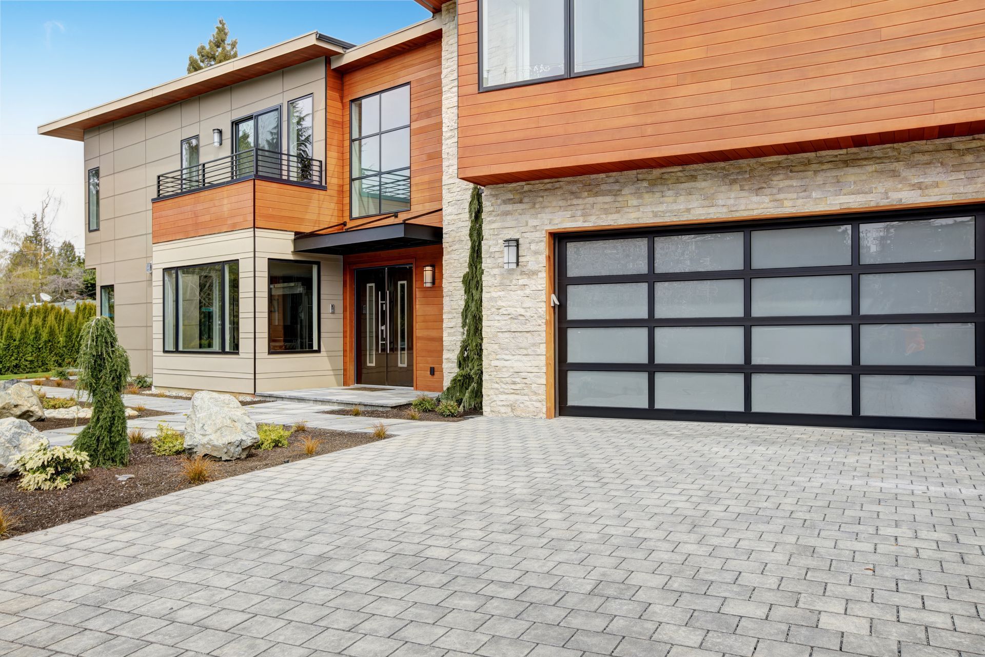 Modern two-story brick house with stone facade, balcony, and large glass garage door.