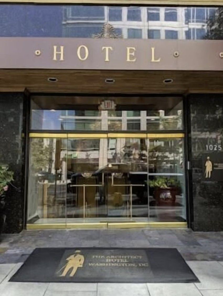 Hotel entrance with glass doors, gold accents, and a black doormat. 