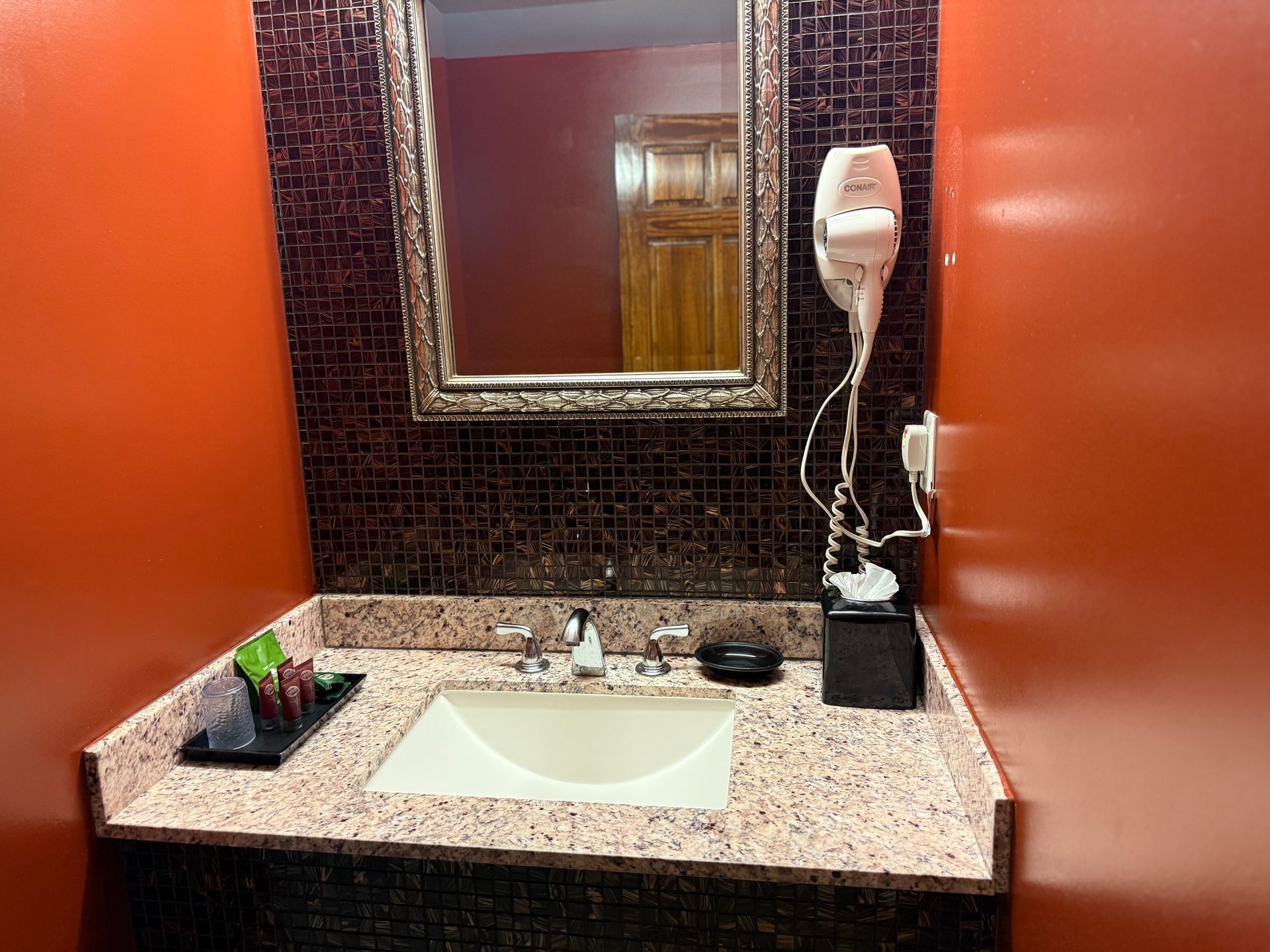 Bathroom with orange walls, mosaic tile backsplash, sink, mirror, and hair dryer.