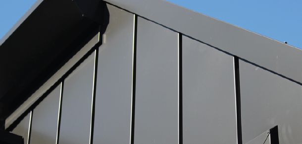 Close-up of a modern gray building facade with black roof trim against a blue sky