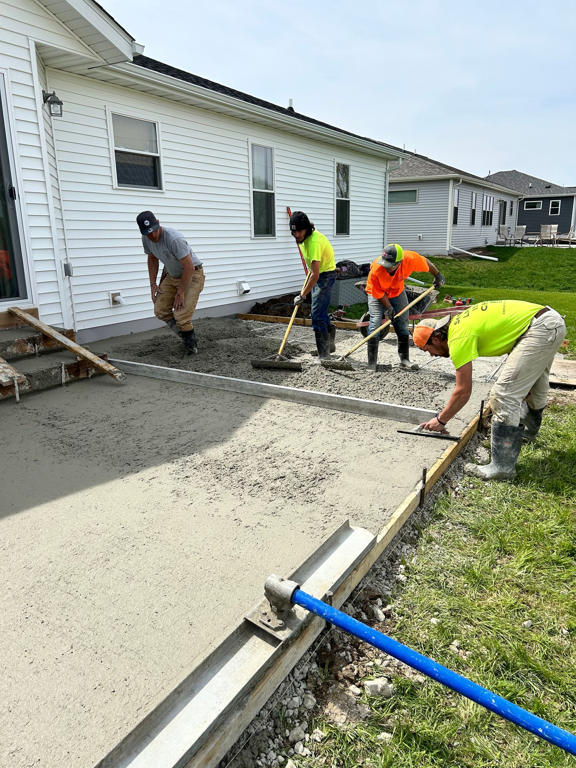 A group of construction workers are working on a sidewalk in front of a house.