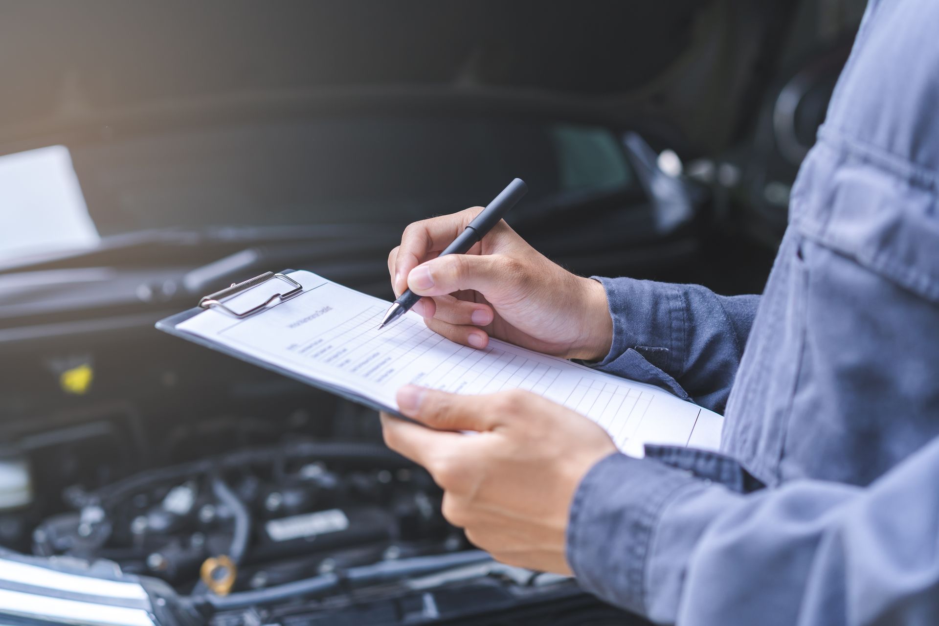 Mechanic in Uniform Inspecting a Car Engine, Writing on A Clipboard — Erina Mechanical Repairs In Erina, NSW