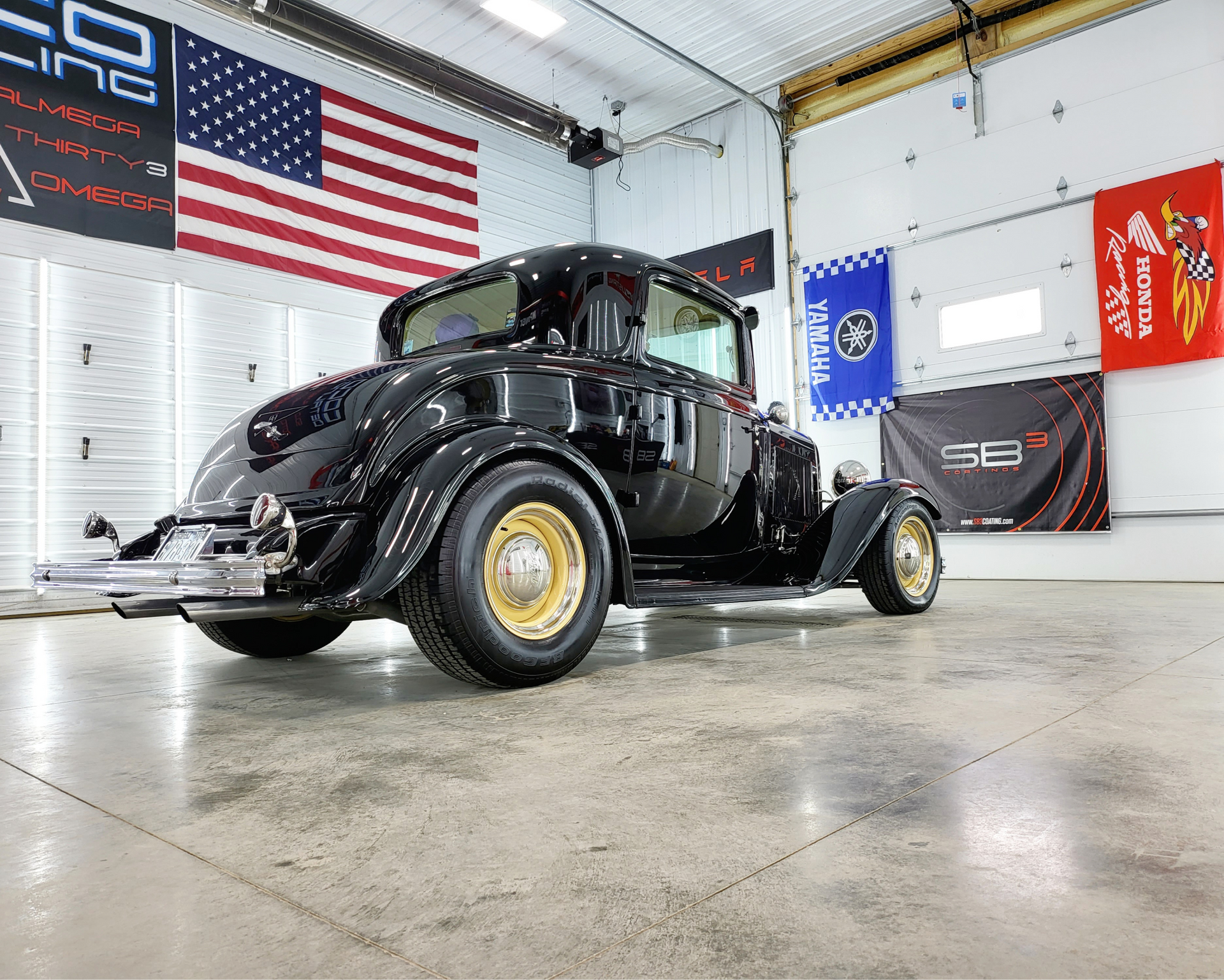 A black car is parked in a garage with flags on the wall.