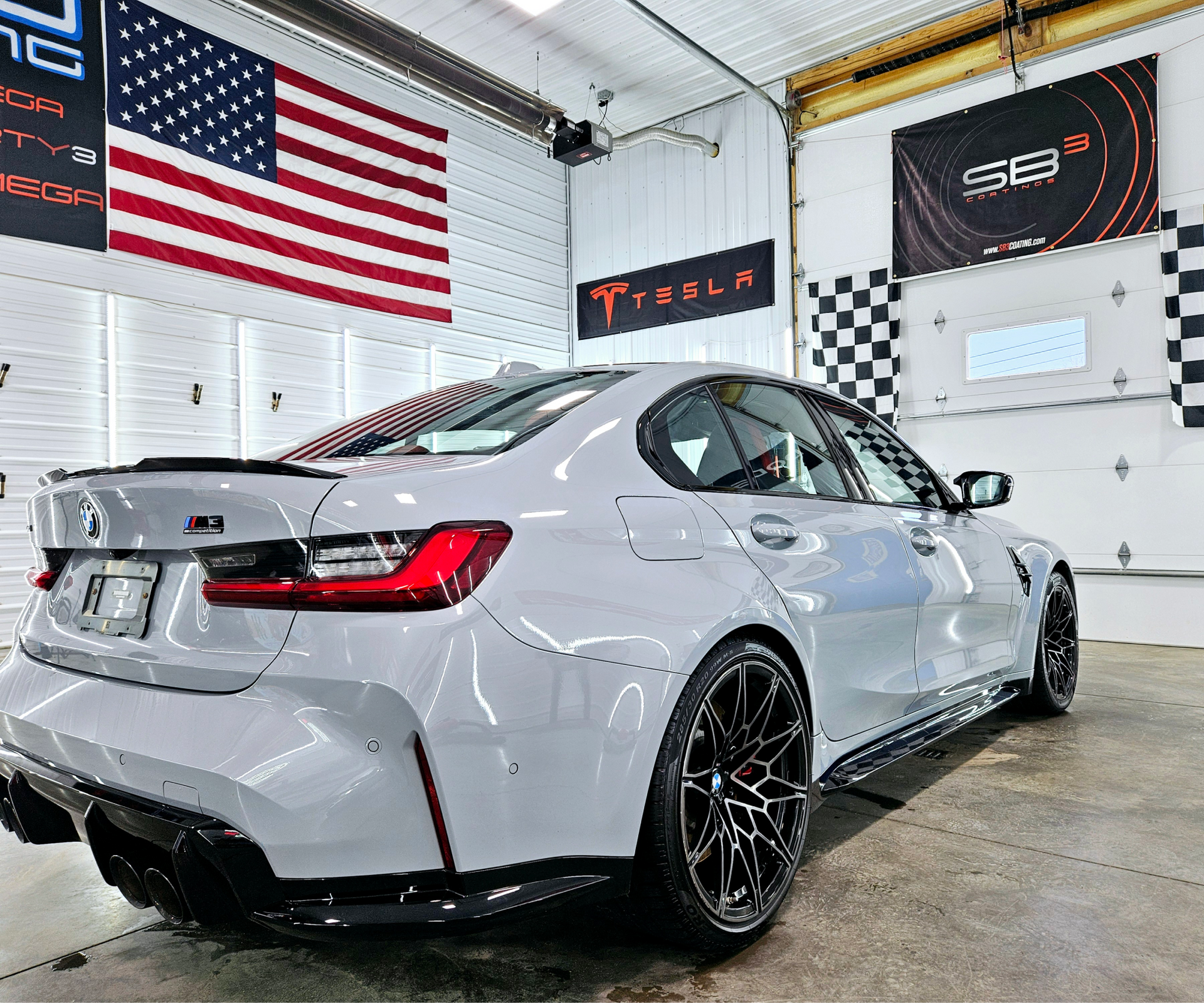 A gray bmw m3 is parked in a garage next to an american flag.