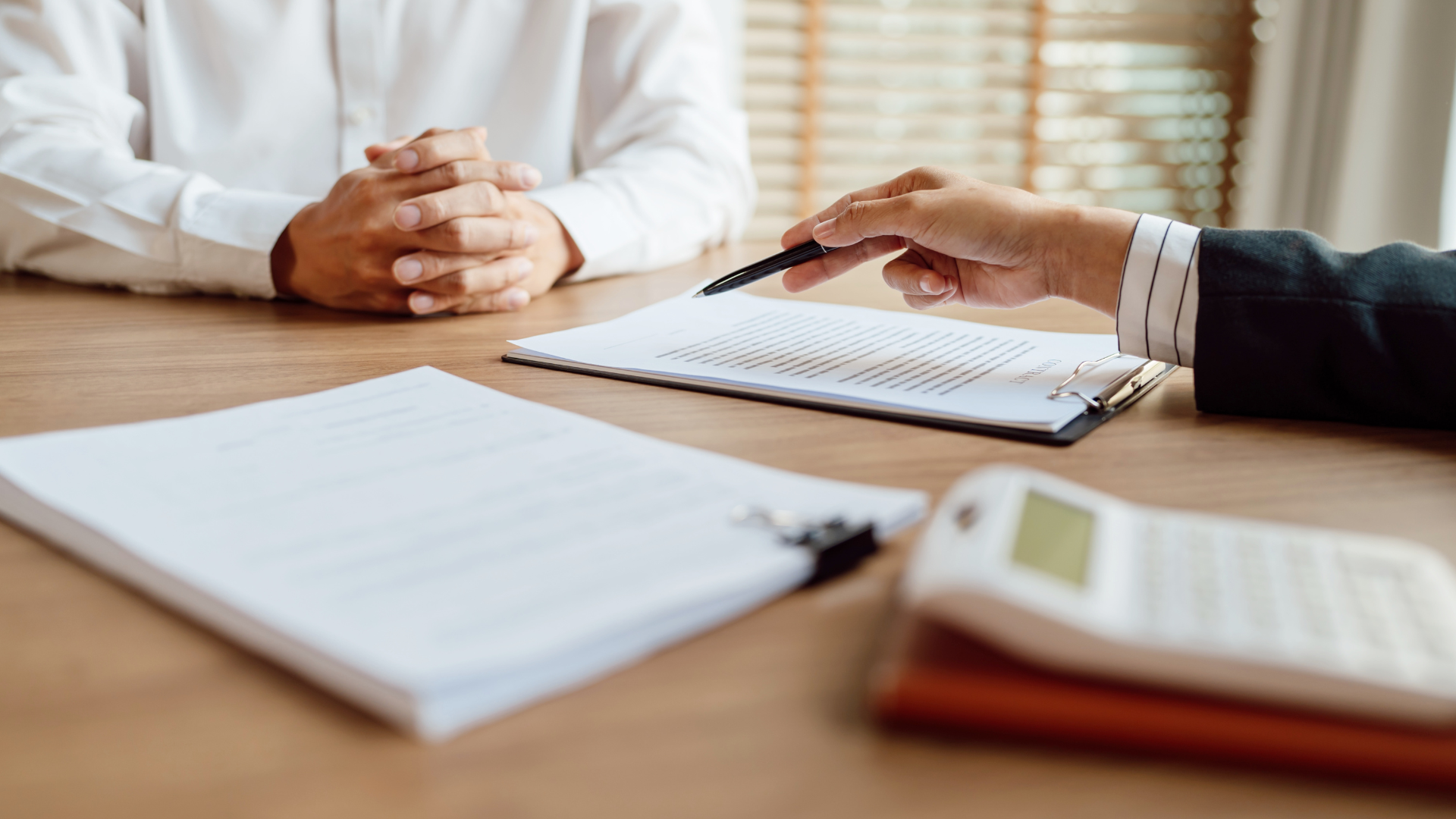 A person reviewing documents with a pen while another person sits at a table, formal setting.