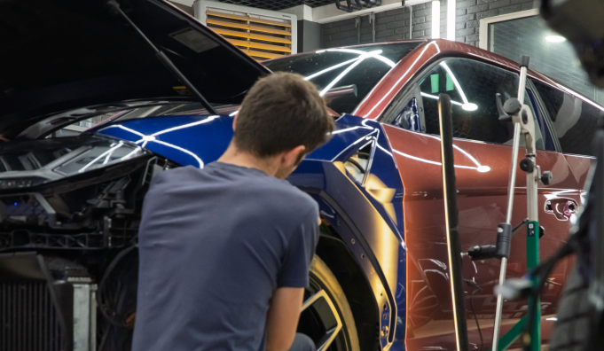 Person working on a blue and red car in a garage with the hood open