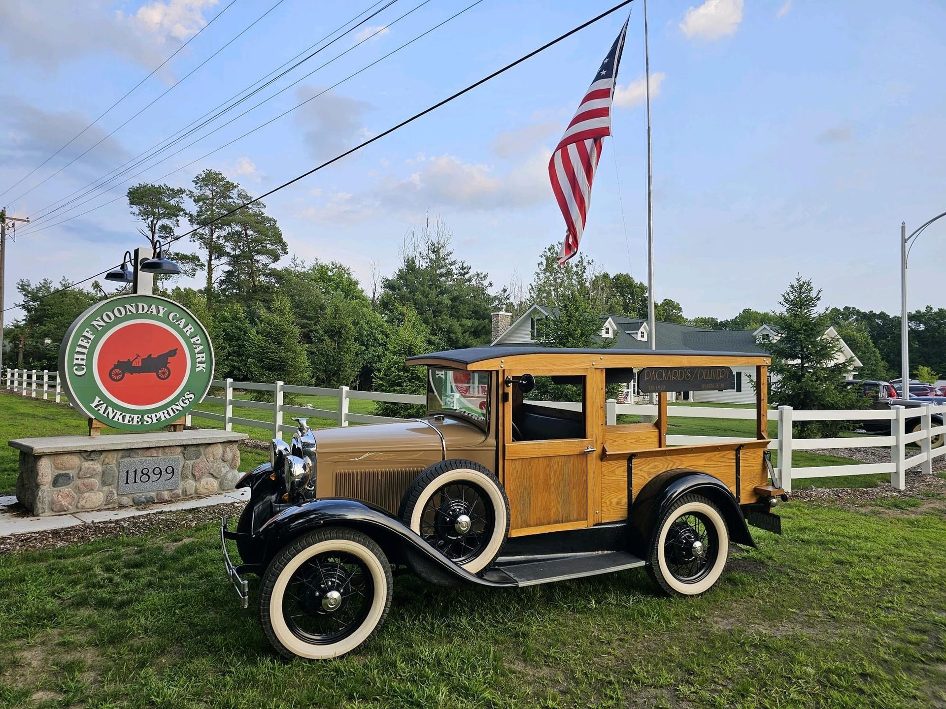 Vintage wood-paneled car parked by a roadside farm sign with an American flag overhead