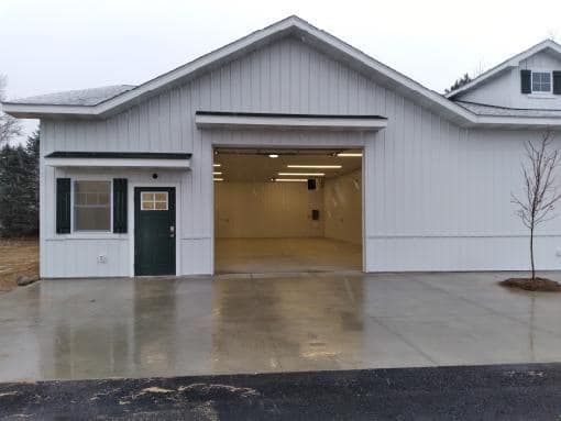 White garage with open bay and green side door on a wet driveway under cloudy skies