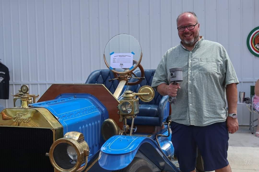 Man smiling beside a blue vintage-style scooter with brass accents indoors