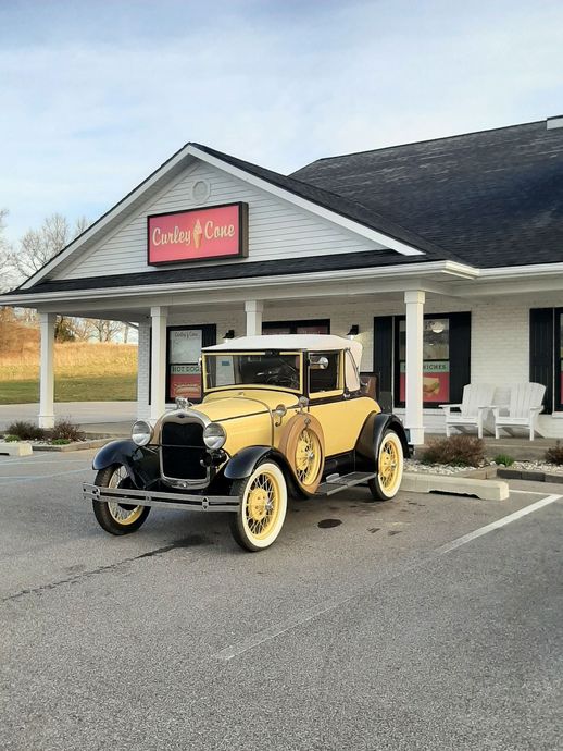 Vintage yellow car parked outside a white building with a red sign and covered porch