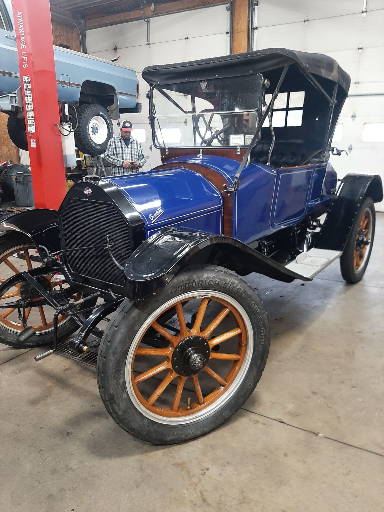 Vintage blue open-top car with wooden-spoke wheels in a garage.