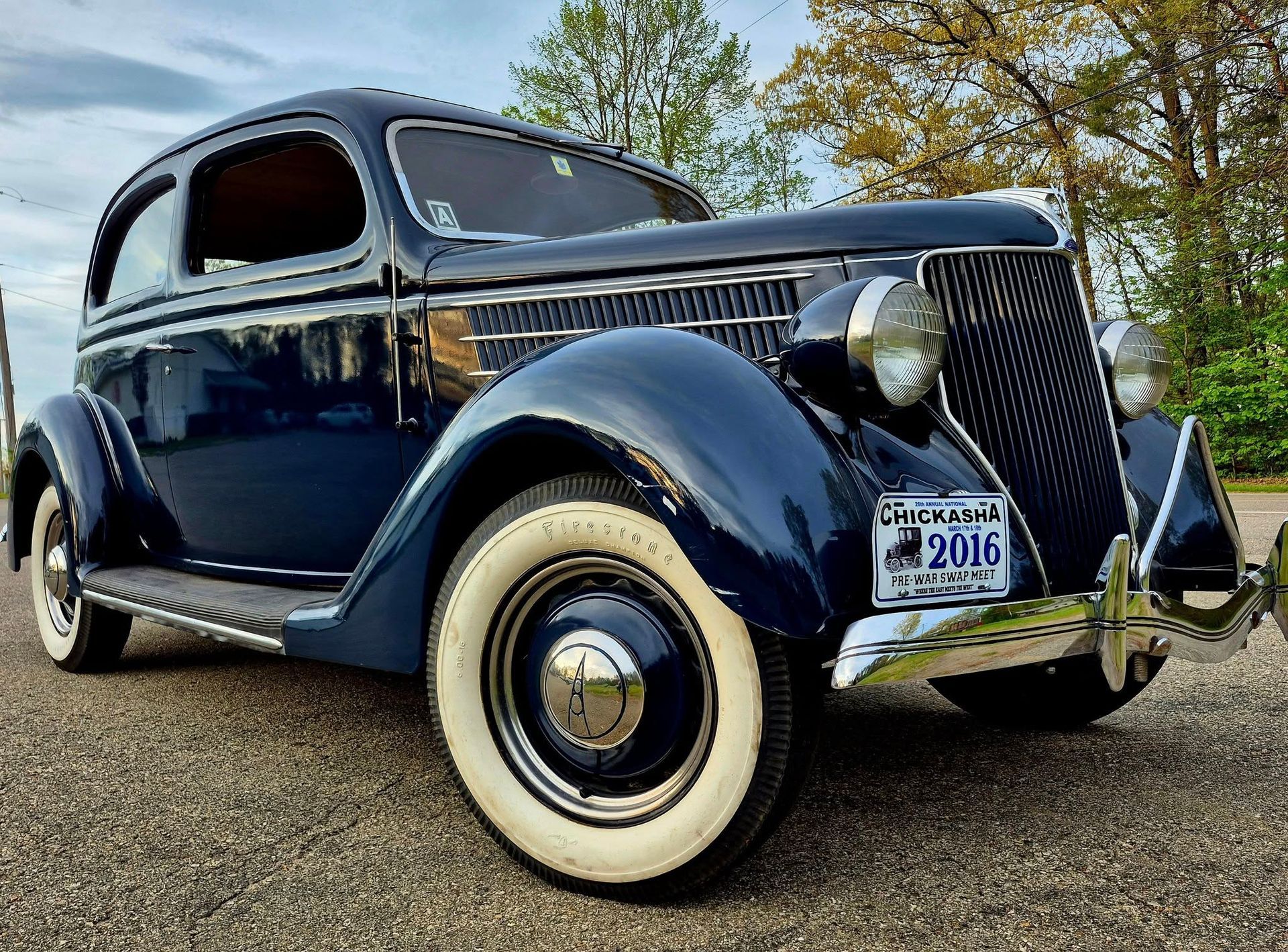 Blue vintage coupe with whitewall tires parked outdoors on a gravel lot