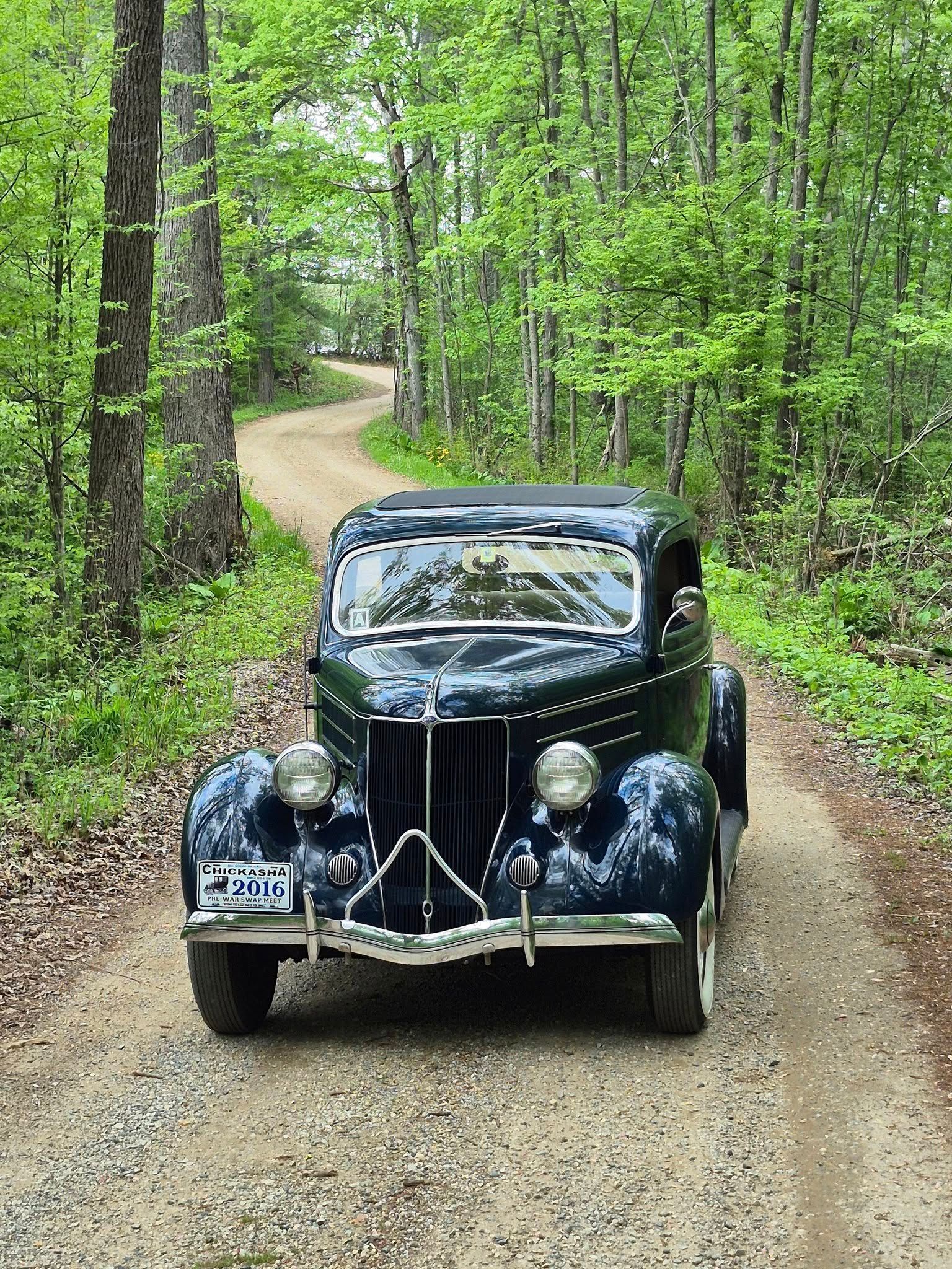 Black vintage car on a winding dirt road through a green forest.