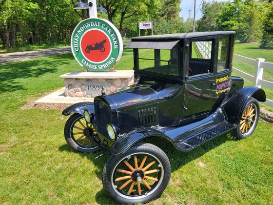 Black vintage car on grass beside a route sign in a sunny park