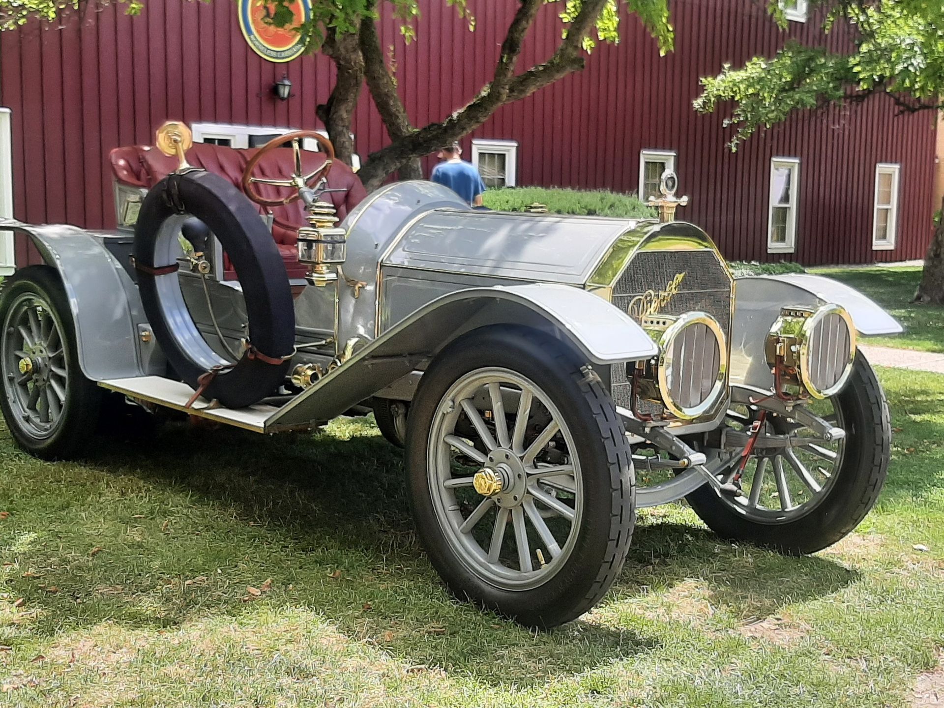 Vintage silver convertible car parked on grass in front of a red barn