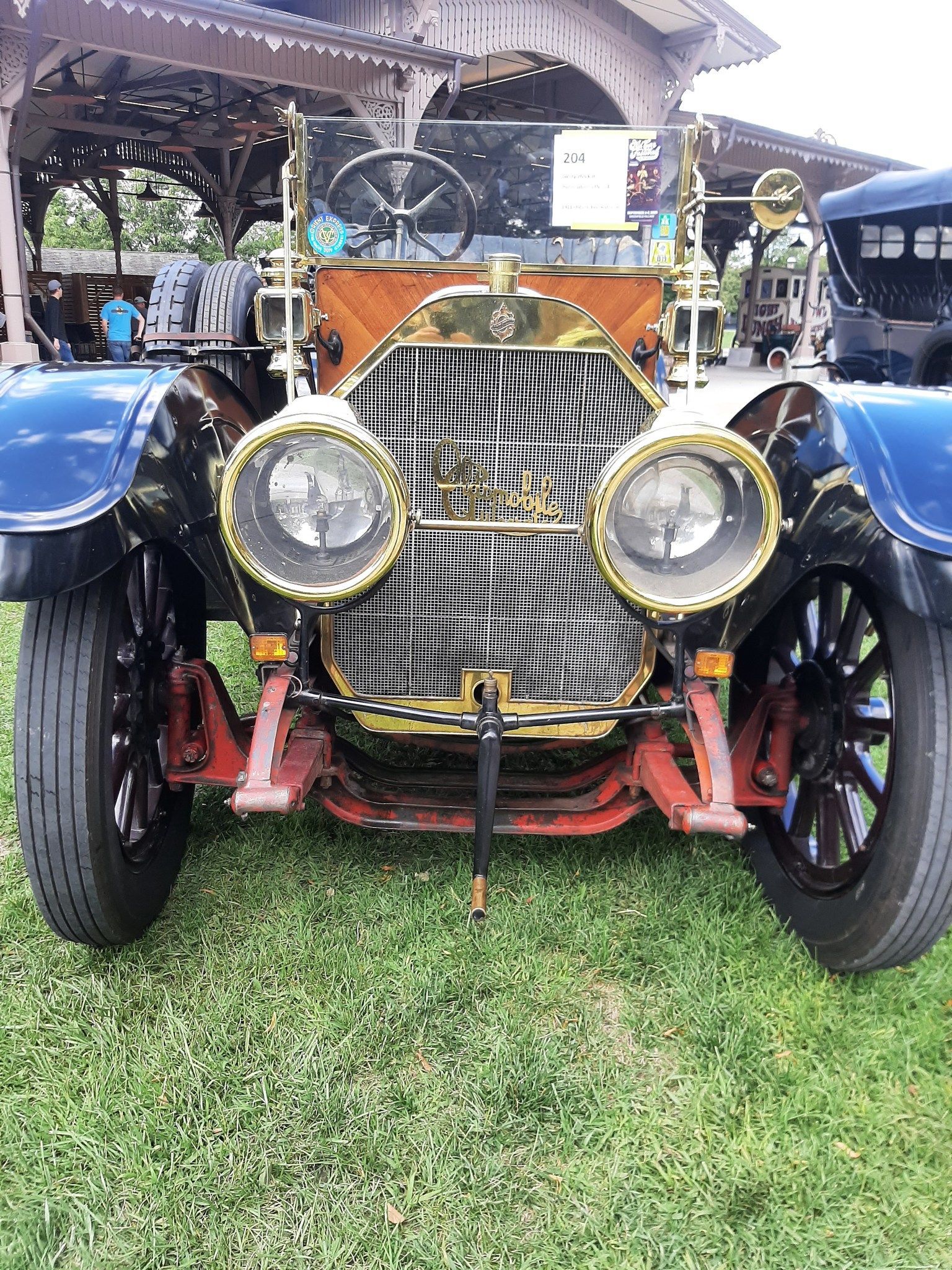 Front view of a vintage blue car with large round headlights and gold grille at an outdoor show.
