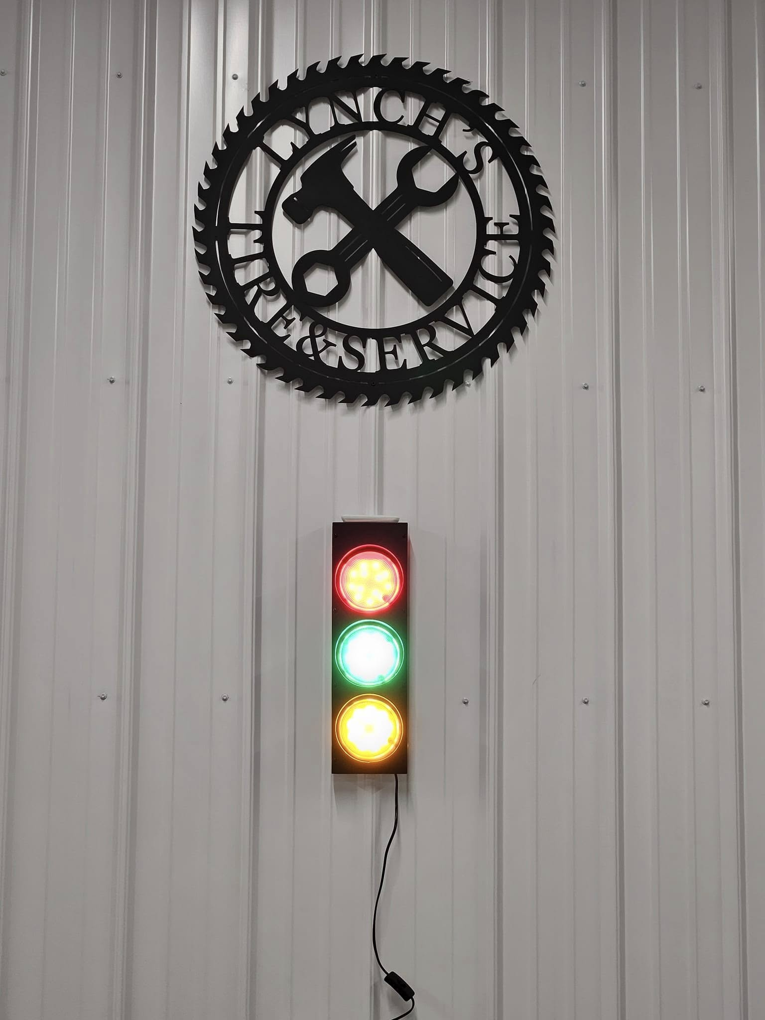 Traffic light-style sign with red, green, and amber lights below a black gear logo on a corrugated wall.