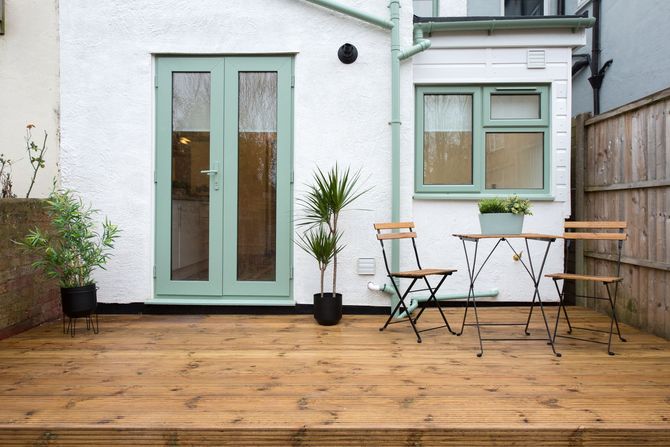 A wooden deck with a table and chairs in front of a house. A wooden deck with a table and chairs in front of a house.