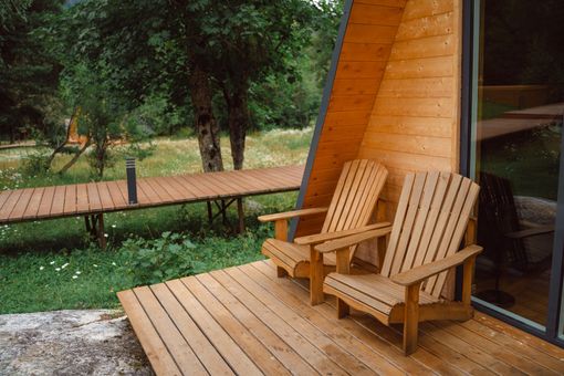 Two wooden chairs are sitting on a wooden deck in front of a wooden cabin. Two wooden chairs are sitting on a wooden deck in front of a wooden cabin.