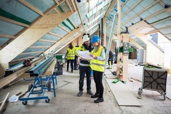 A man and a woman are standing in a building under construction looking at a blueprint. A man and a woman are standing in a building under construction looking at a blueprint.