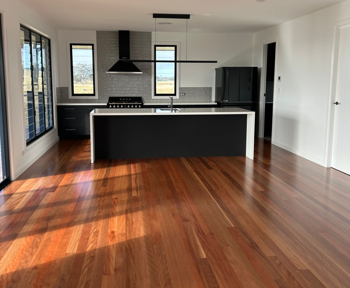 Kitchen with hardwood floors, dark cabinets, a white island, and large windows — C & S Building In Bentley, NSW