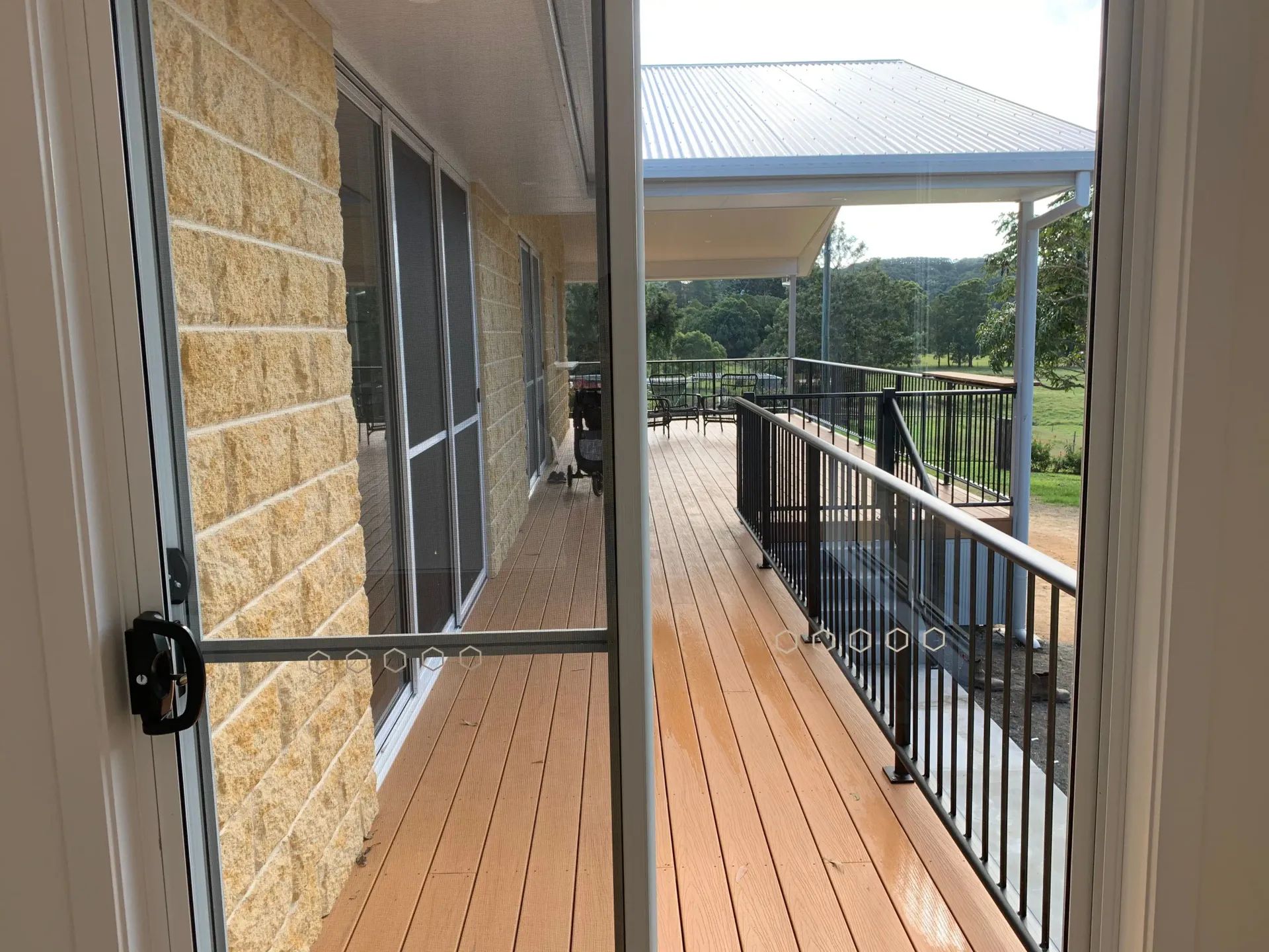 View from inside a house to a wooden deck with black railing and covered patio — C & S Building In Bentley, NSW