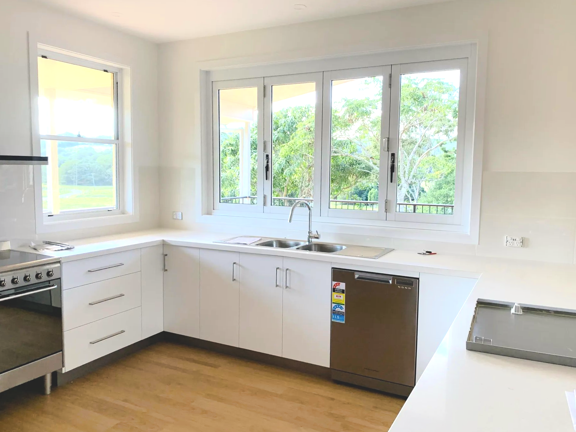 White kitchen with a stove, sink, dishwasher, and large windows — C & S Building In Bentley, NSW