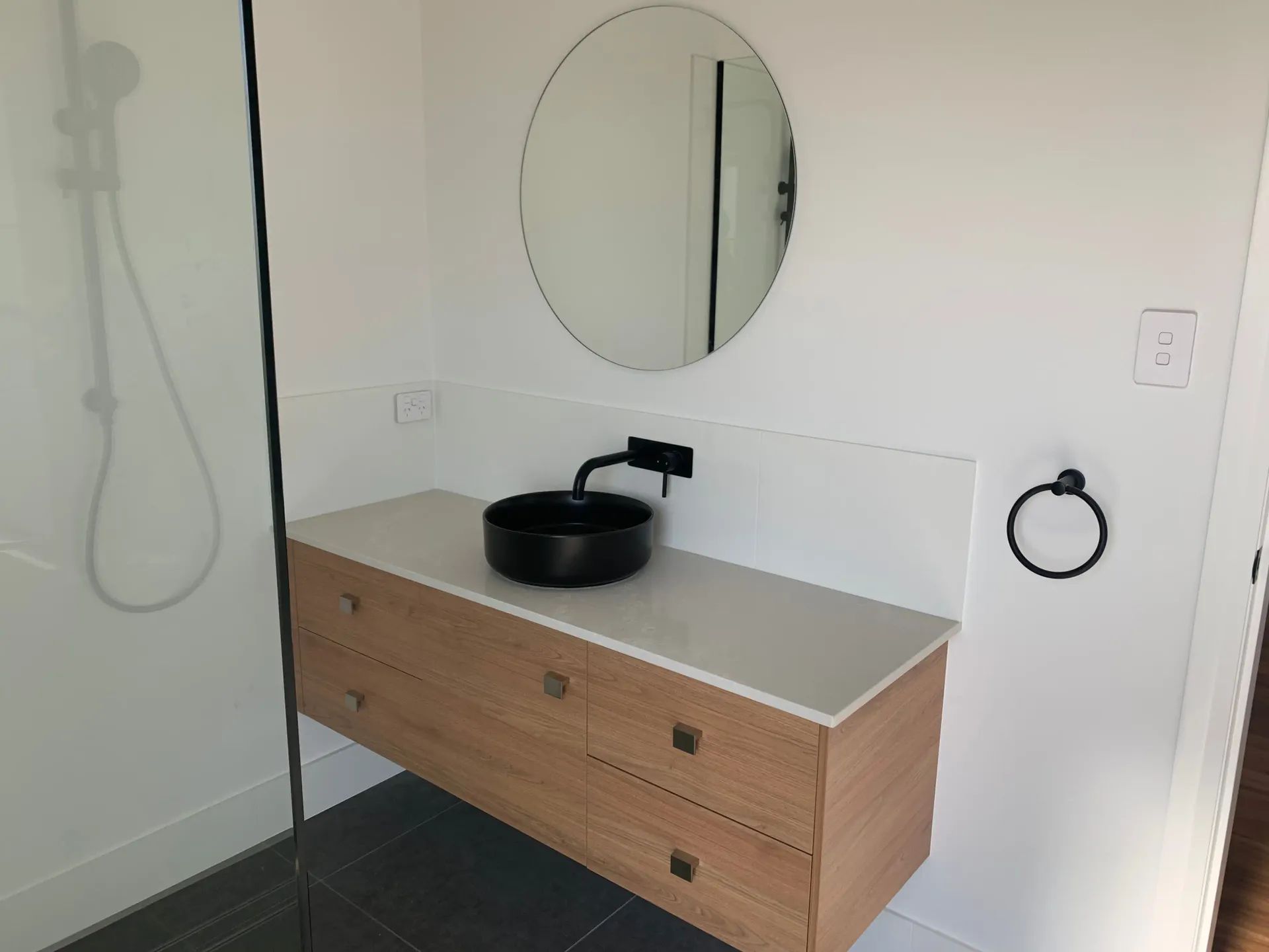 Floating Wooden Vanity with Black Sink and Round Mirror in A Bathroom — C & S Building In Bentley, NSW