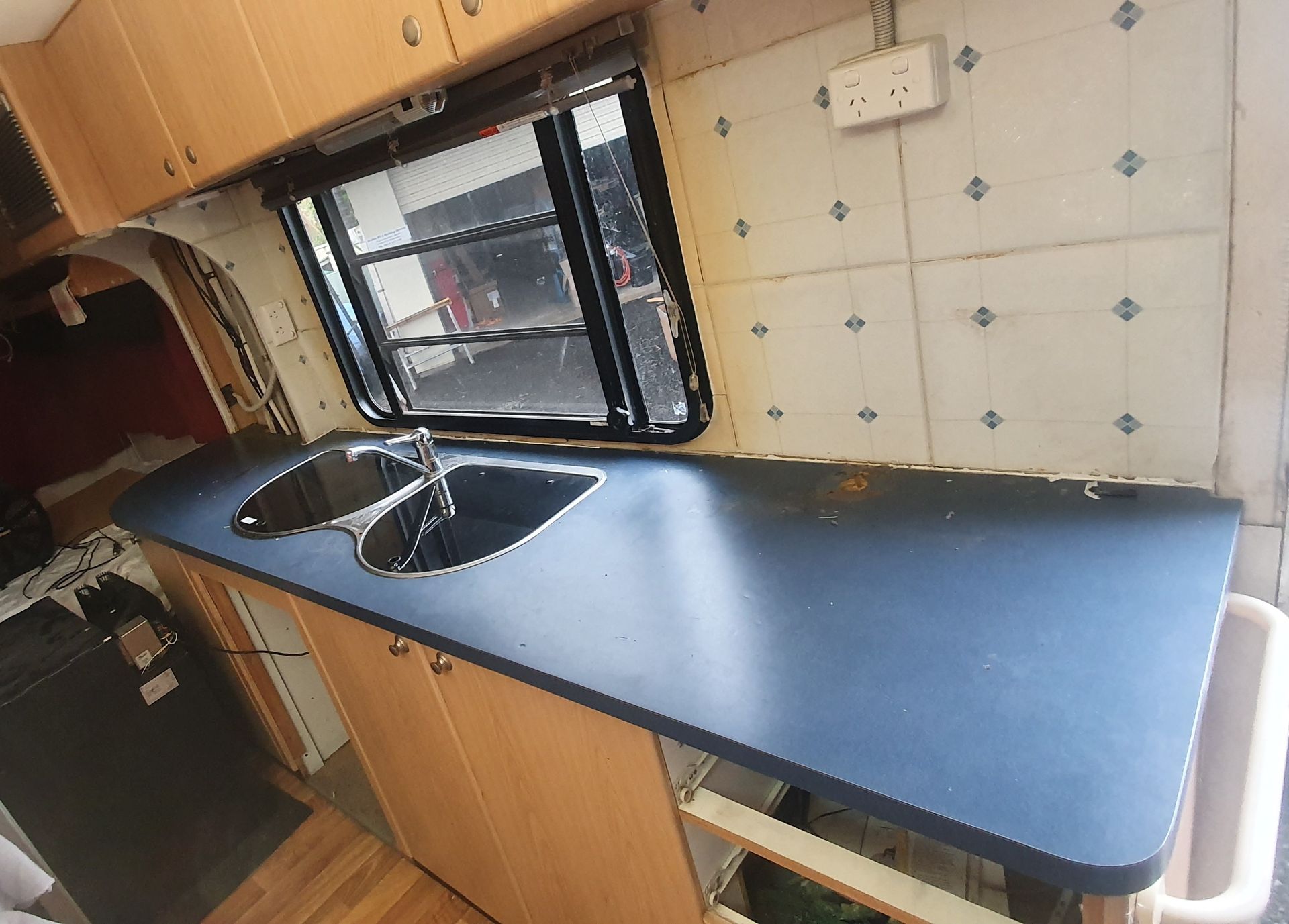 Interior of a campervan kitchen with a dark blue countertop, sink, and cabinets. A window and tiled wall are also visible.