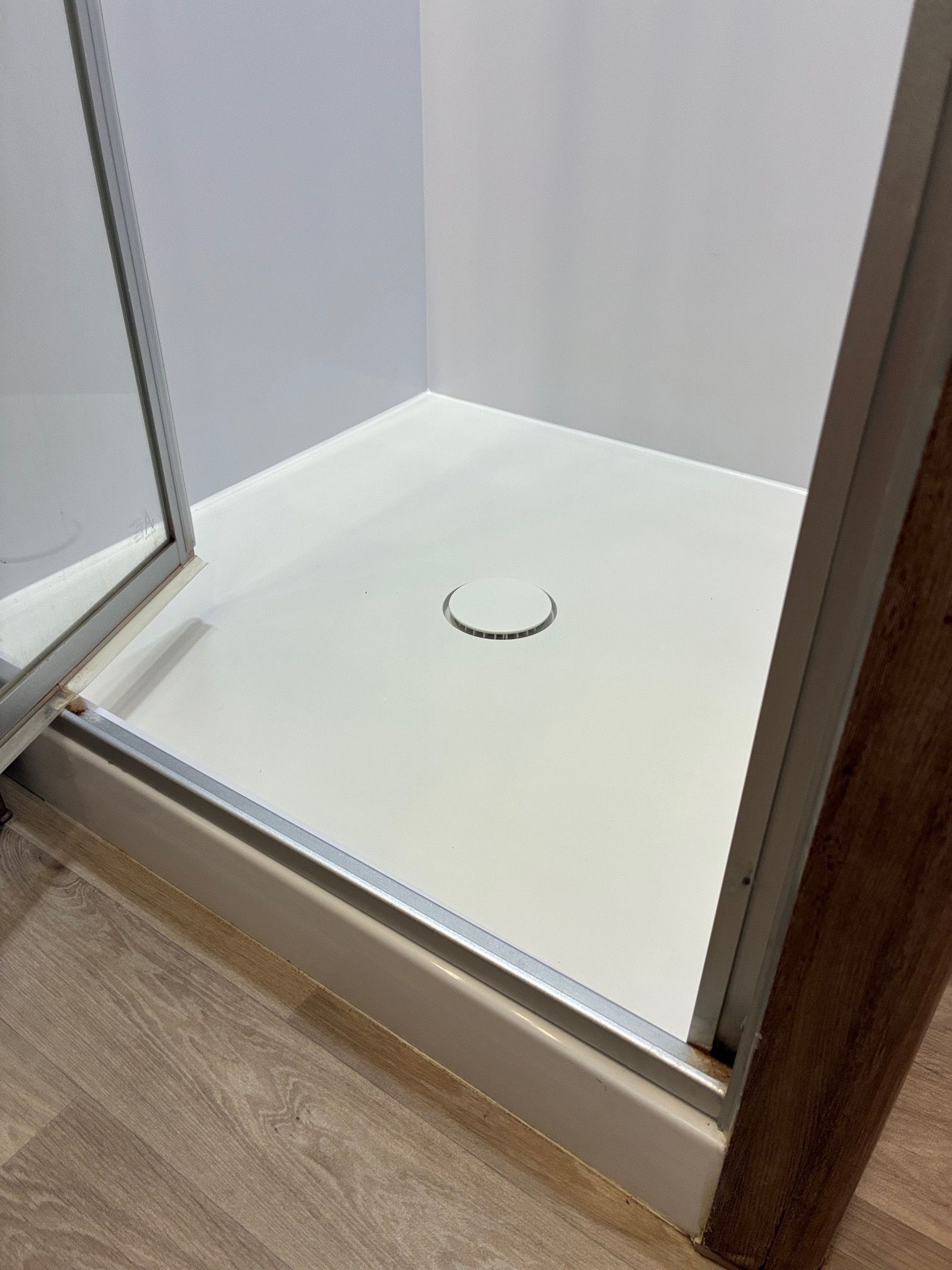 Red Fox installing a White shower stall with a drain, sliding glass door, and wood-look flooring.