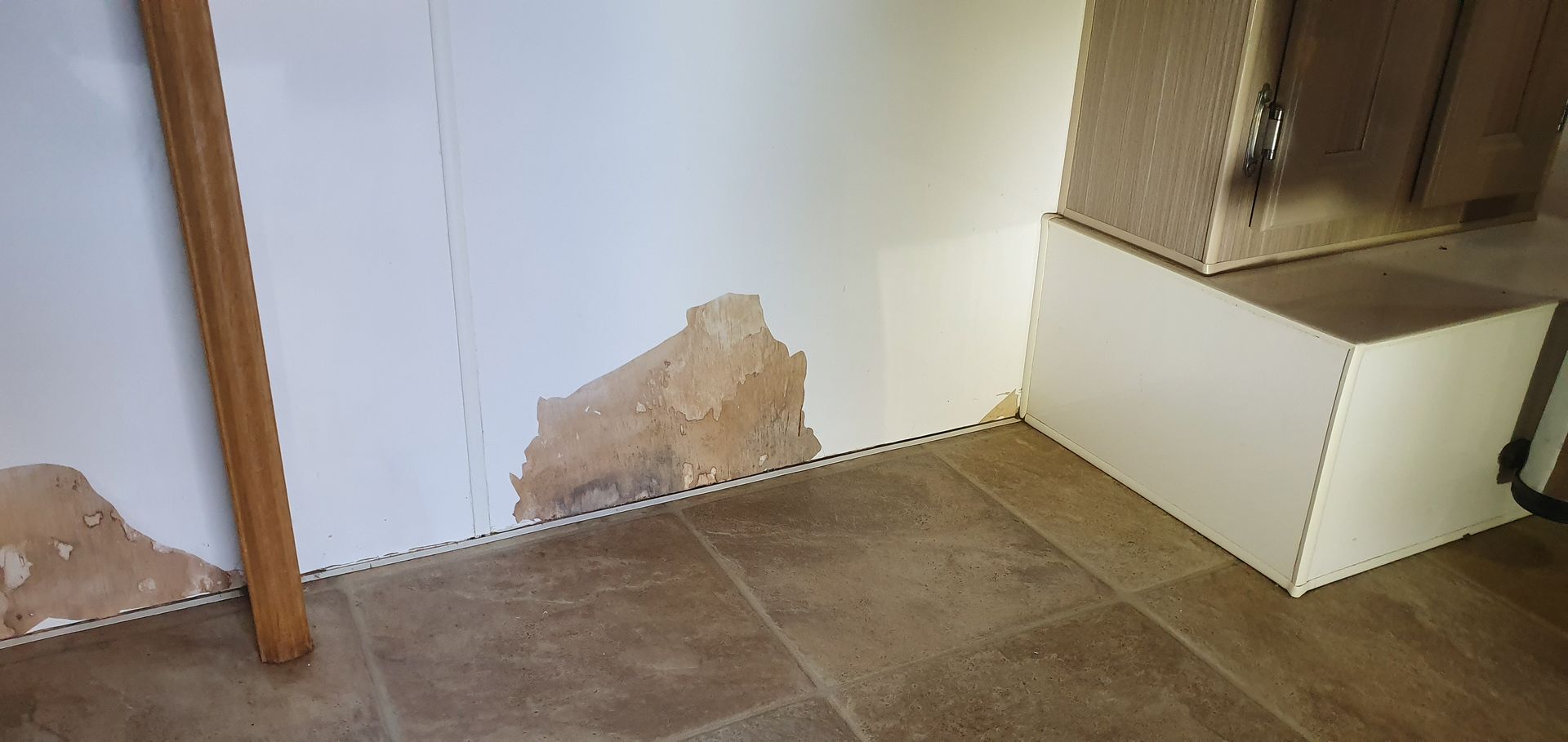 Damaged drywall along the floor, next to a wood support and an off-white box.