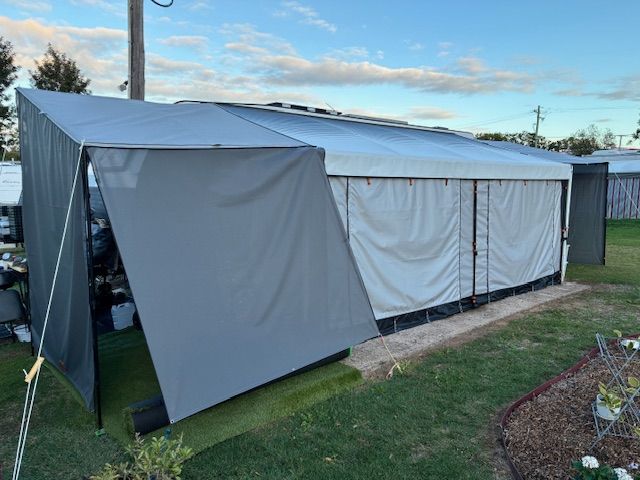 Grey and white camper trailer with awning set up on green grass.