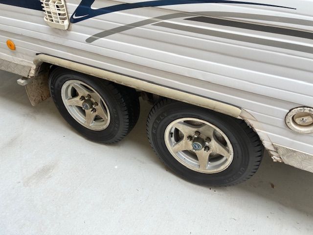 Side view of a silver travel trailer with two tires and wheels.