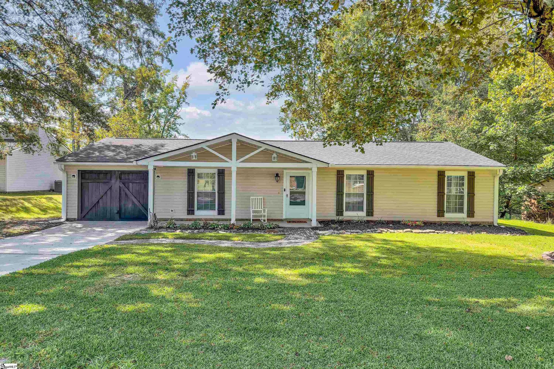 Single-story yellow house with a front porch, garage, and large green lawn under trees
