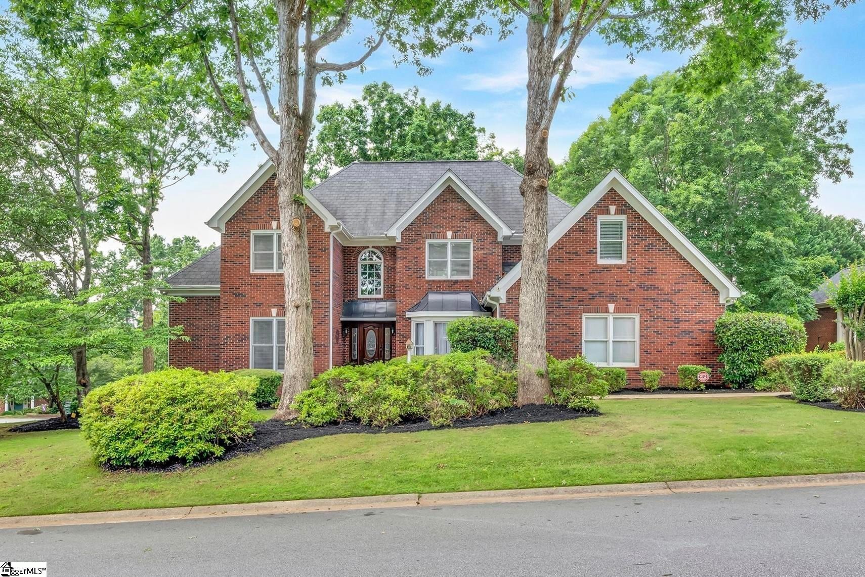 Brick suburban house with white trim, manicured lawn, and tall trees along the street