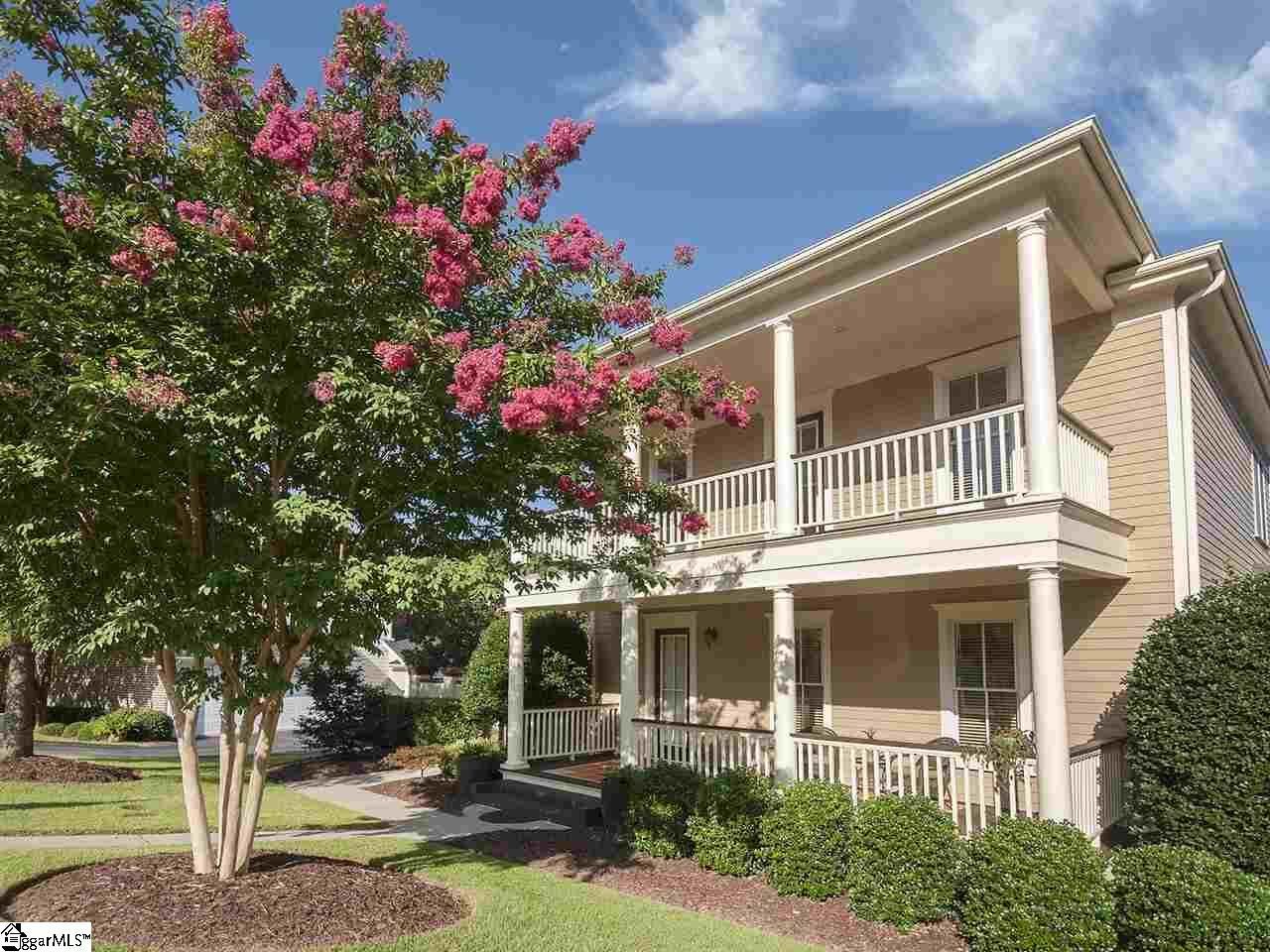 Two-story brick house with white porch columns and pink flowering trees in front yard