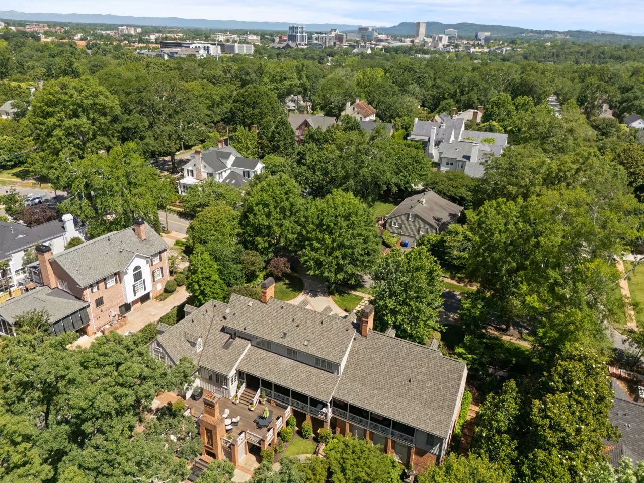 Aerial view of a leafy residential neighborhood with houses, trees, and a city skyline in the distance.