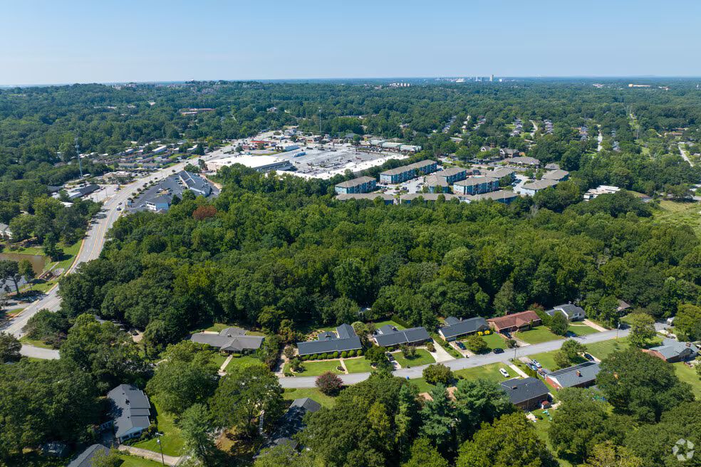 Aerial view of a leafy suburban neighborhood with houses, roads, and a large shopping center in the distance