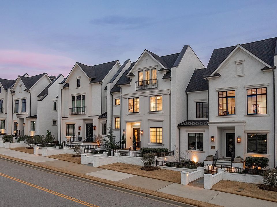 Row of modern white townhouses with lit windows along a quiet street at dusk