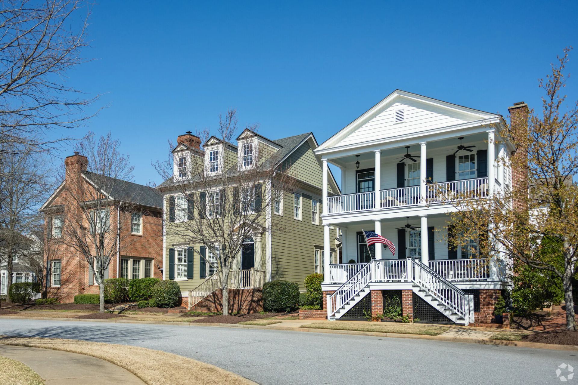 Row of historic homes with porches on a quiet street under a clear blue sky