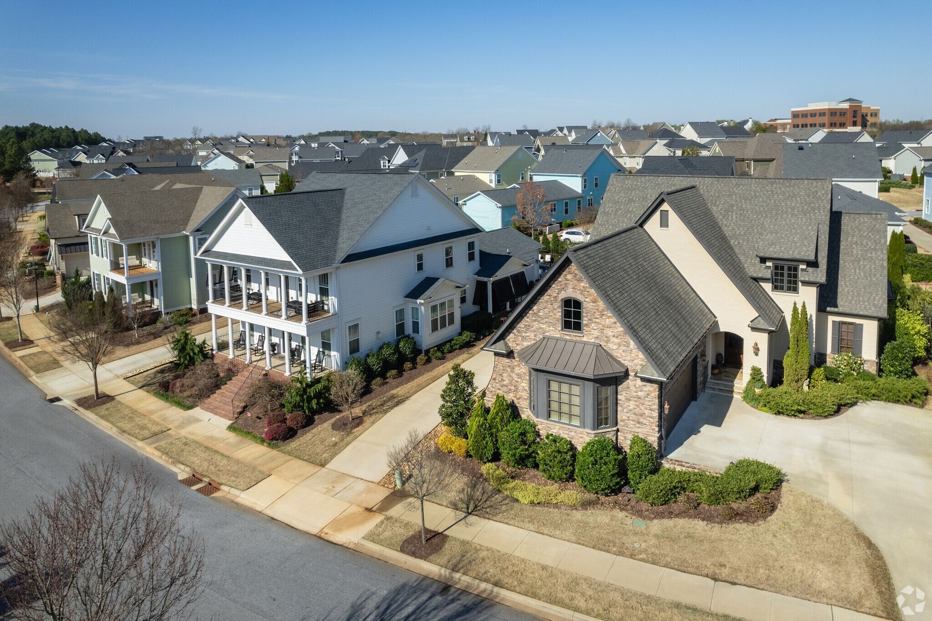 Suburban neighborhood with modern houses, gray roofs, and a wide street under a clear blue sky